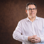 Portrait professionnel de Didier Lourdelle, consultant et formateur, regard face caméra, fond brun.